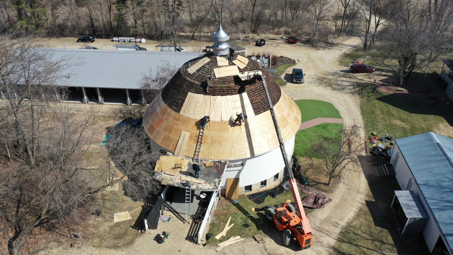 Aerial drone view of crew installing new plywood decking on the round barn roof